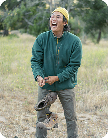 uomo sorridente in mezzo alla natura con in mano scarponcino keen targhee