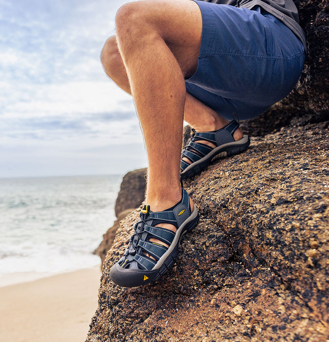 dettaglio sandali keen newport navy indossati da un uomo sugli scogli in riva al mare
